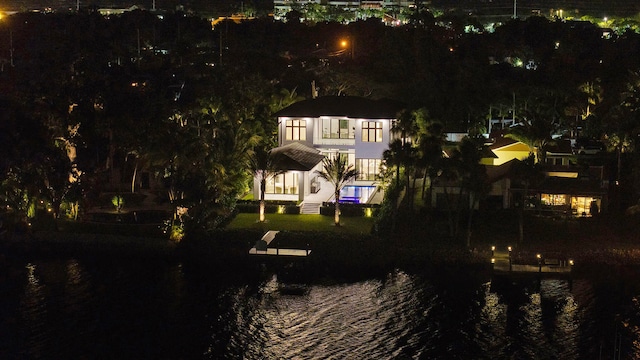 back house at night with a water view, a lawn, and a balcony