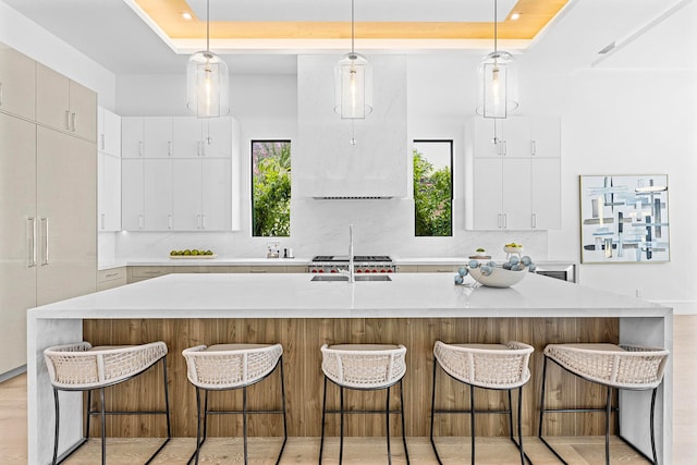 kitchen with a tray ceiling, decorative backsplash, a center island with sink, and hanging light fixtures