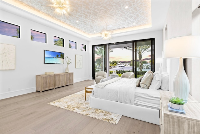 bedroom with light hardwood / wood-style floors, a raised ceiling, and a notable chandelier