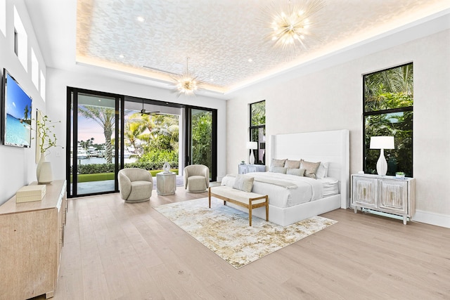 bedroom featuring access to exterior, a raised ceiling, light wood-type flooring, and a notable chandelier