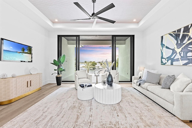 living room with light wood-type flooring, ceiling fan, and a raised ceiling