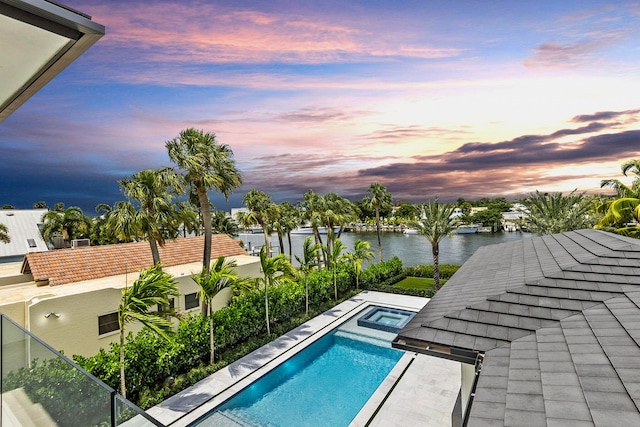 pool at dusk featuring a water view and an in ground hot tub