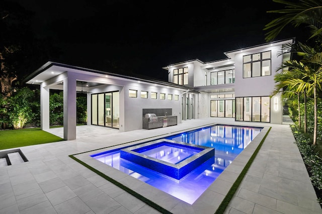 pool at twilight with area for grilling, an in ground hot tub, and a patio area