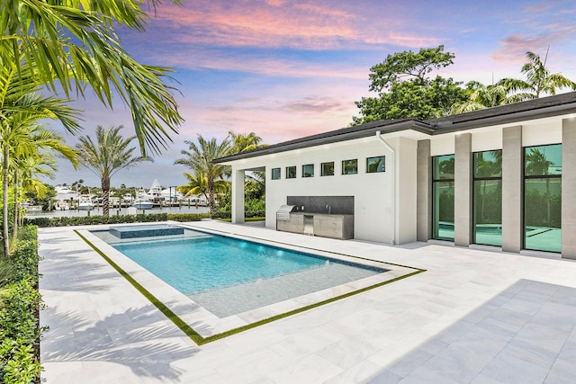 pool at dusk featuring a patio area, an in ground hot tub, and exterior kitchen