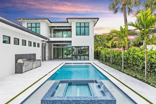 back house at dusk featuring area for grilling, a pool with hot tub, sink, and a patio area