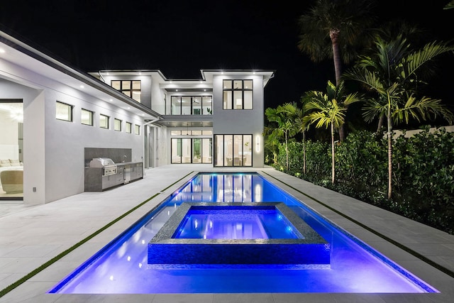 pool at night featuring an outdoor kitchen, a patio, and an in ground hot tub