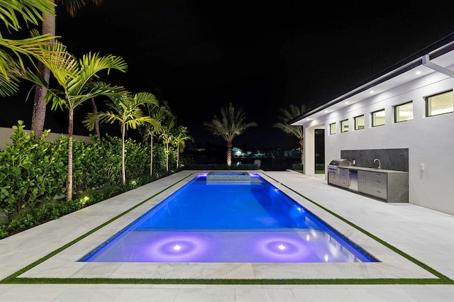 pool at night with an outdoor kitchen, a hot tub, and a patio area