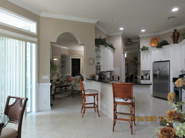 kitchen with ornamental molding, stainless steel refrigerator with ice dispenser, a breakfast bar, white cabinets, and kitchen peninsula