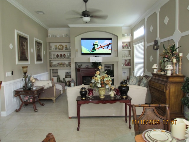 living room featuring built in shelves, light tile patterned flooring, ceiling fan, and crown molding