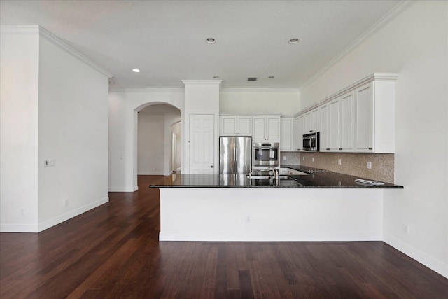 kitchen featuring stainless steel appliances, dark wood-type flooring, white cabinets, kitchen peninsula, and decorative backsplash