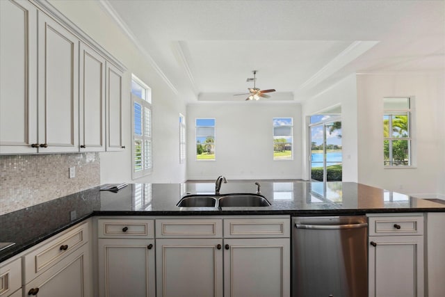 kitchen featuring sink, dark stone countertops, stainless steel dishwasher, a tray ceiling, and ceiling fan