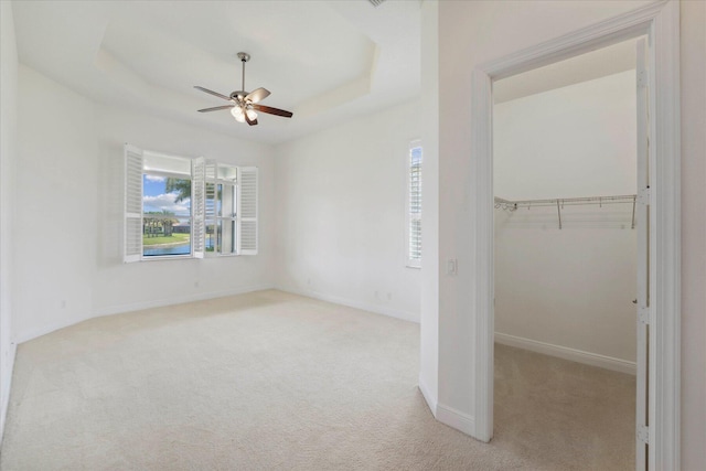 unfurnished bedroom with ceiling fan, a raised ceiling, a closet, and light colored carpet