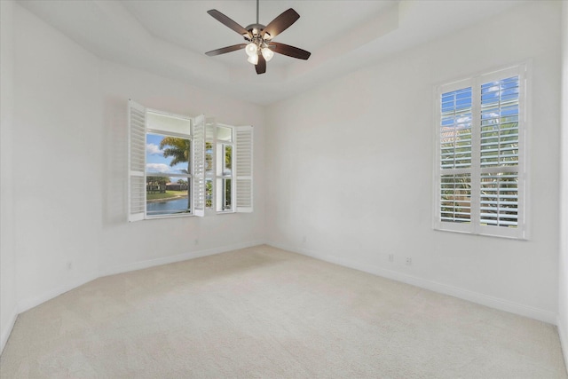 carpeted empty room with plenty of natural light, ceiling fan, and a tray ceiling