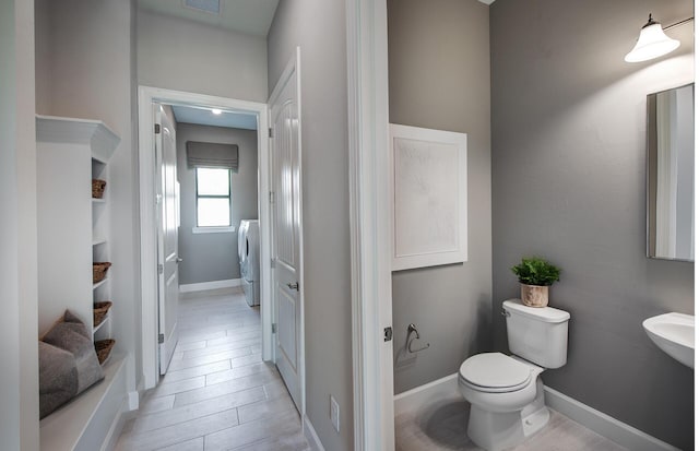 bathroom featuring visible vents, baseboards, toilet, wood finished floors, and washer and dryer