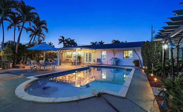 pool at dusk with a patio area and grilling area