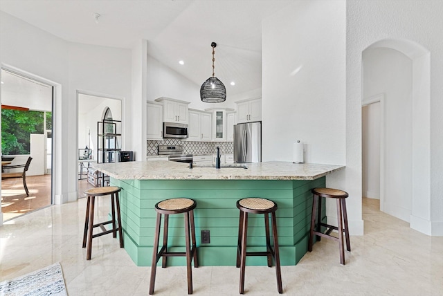 kitchen with a kitchen bar, appliances with stainless steel finishes, kitchen peninsula, white cabinetry, and hanging light fixtures