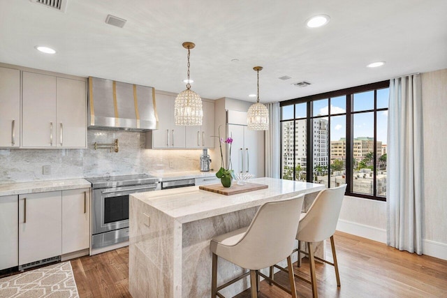 kitchen featuring pendant lighting, wall chimney range hood, stainless steel electric range oven, light hardwood / wood-style floors, and light stone counters