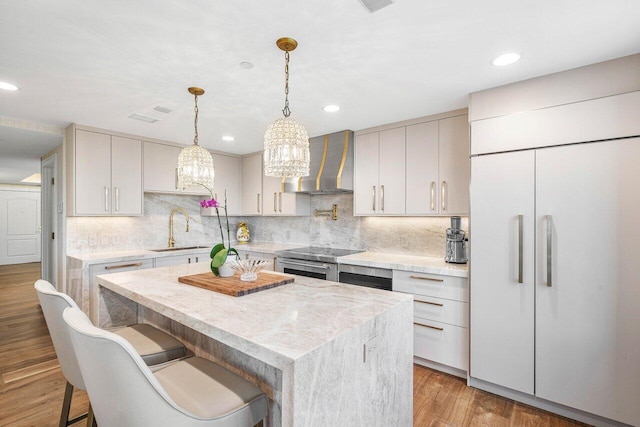 kitchen with a kitchen breakfast bar, wall chimney range hood, sink, paneled refrigerator, and light hardwood / wood-style floors