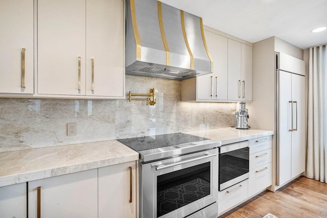 kitchen with tasteful backsplash, light hardwood / wood-style flooring, wall chimney range hood, and appliances with stainless steel finishes