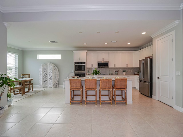 kitchen featuring an island with sink, white cabinetry, appliances with stainless steel finishes, and a kitchen bar