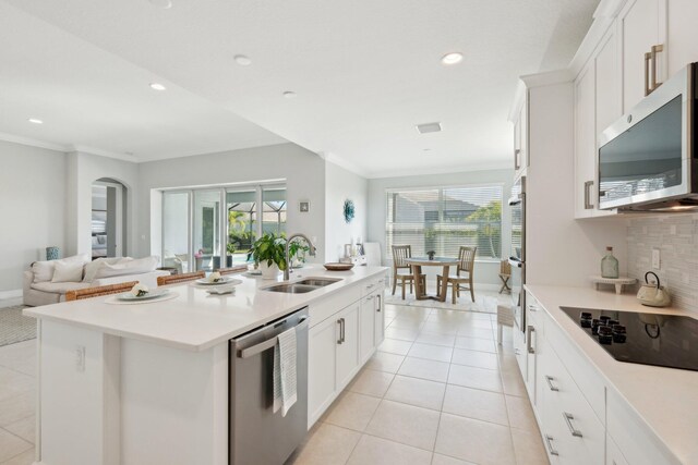 kitchen with stainless steel appliances, a center island with sink, white cabinetry, a kitchen bar, and crown molding