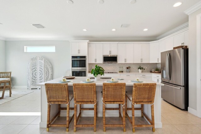 kitchen with stainless steel appliances, white cabinets, a kitchen island with sink, ornamental molding, and a breakfast bar