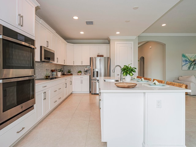 kitchen with stainless steel appliances, white cabinetry, sink, and a kitchen island with sink