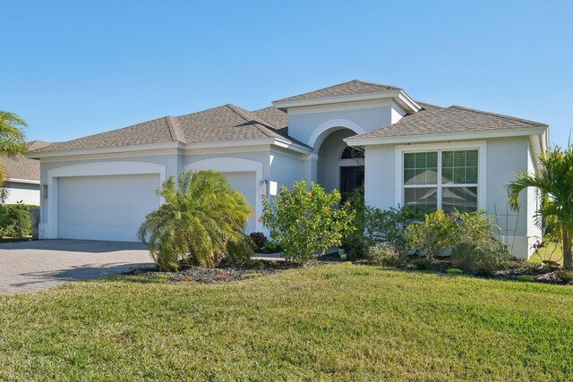 view of front of house with decorative driveway, a front yard, an attached garage, and stucco siding