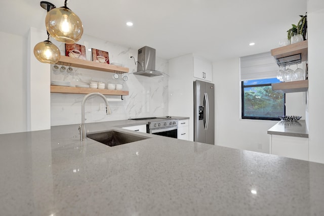 kitchen with white cabinets, wall chimney range hood, sink, appliances with stainless steel finishes, and decorative light fixtures