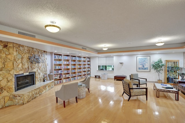 living room with a textured ceiling, hardwood / wood-style flooring, and a stone fireplace