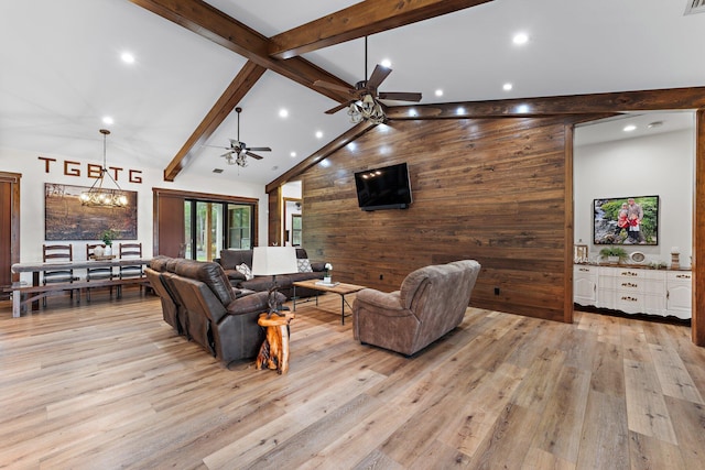 living room with ceiling fan with notable chandelier, wooden walls, high vaulted ceiling, beamed ceiling, and light hardwood / wood-style floors