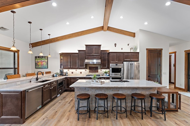 kitchen featuring a kitchen breakfast bar, stainless steel appliances, sink, decorative light fixtures, and beamed ceiling