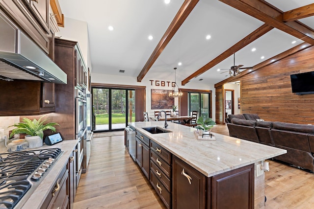 kitchen with sink, a large island with sink, wood walls, pendant lighting, and stainless steel gas stovetop