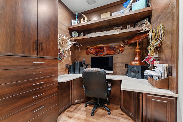 office space with wooden walls, light hardwood / wood-style flooring, and built in desk