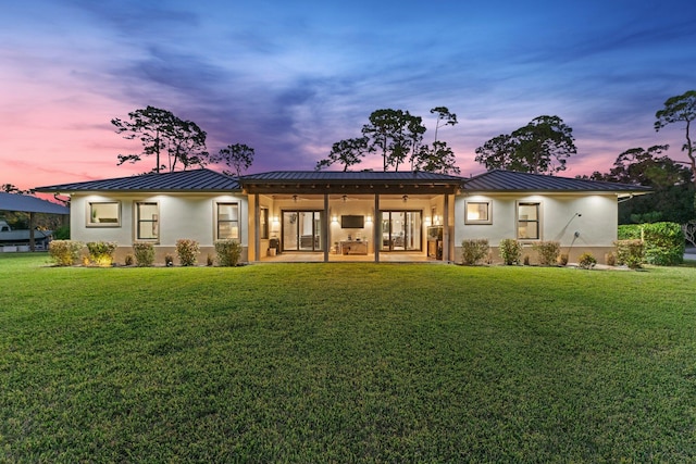 back house at dusk featuring a lawn and ceiling fan