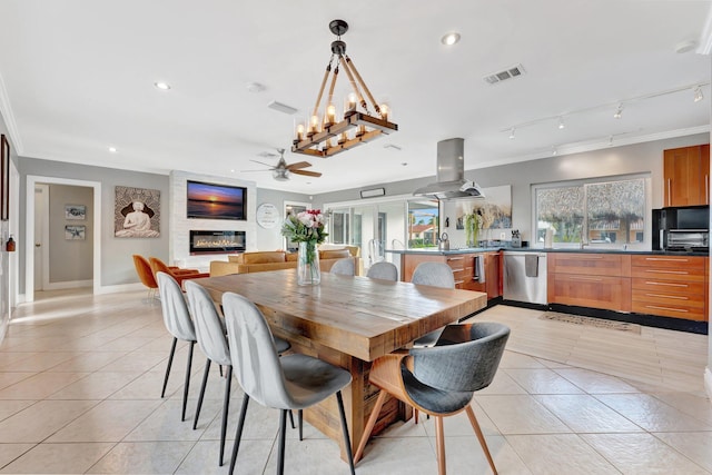 dining space featuring rail lighting, ornamental molding, ceiling fan with notable chandelier, a large fireplace, and light tile patterned floors