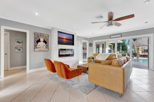 living room featuring ceiling fan, a large fireplace, light tile patterned floors, and crown molding