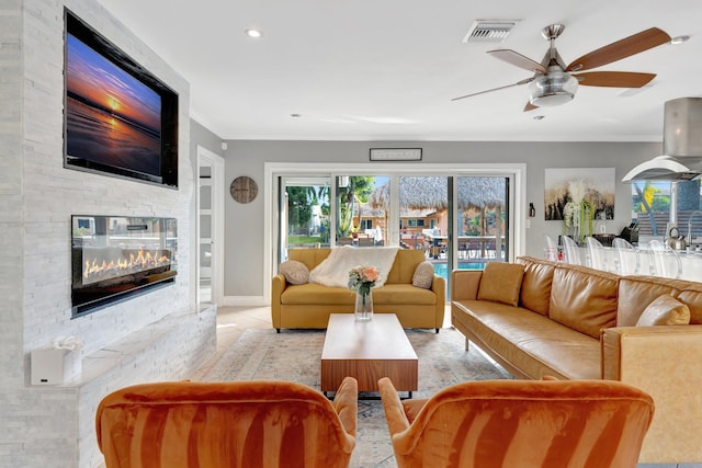 tiled living room featuring a stone fireplace, ceiling fan, and ornamental molding