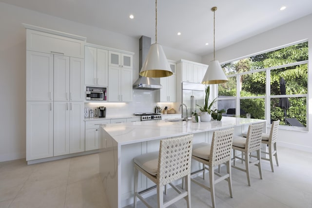 kitchen with sink, wall chimney exhaust hood, stainless steel appliances, decorative light fixtures, and a center island with sink