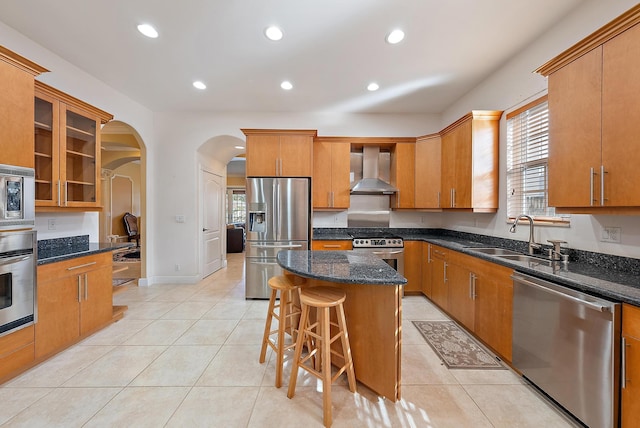 kitchen with sink, wall chimney exhaust hood, stainless steel appliances, light tile patterned floors, and a kitchen island