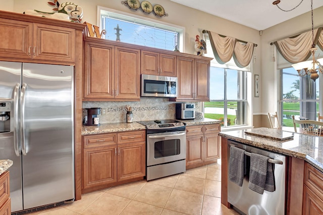 kitchen with pendant lighting, decorative backsplash, light tile patterned floors, appliances with stainless steel finishes, and light stone counters