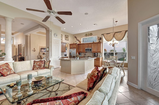 living room featuring light tile patterned floors, ceiling fan with notable chandelier, and ornate columns