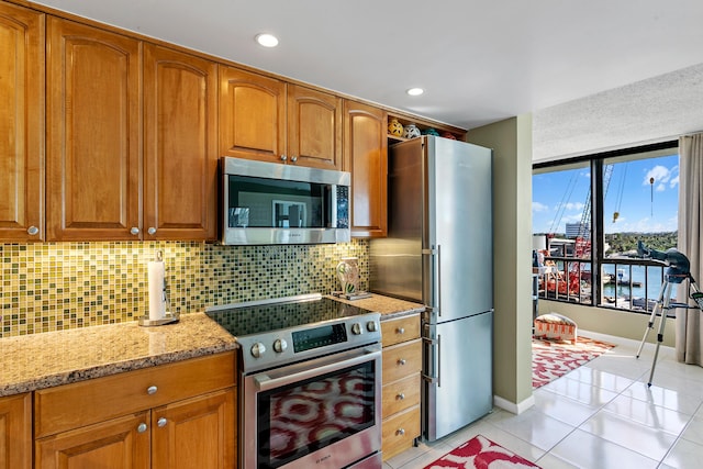 kitchen with appliances with stainless steel finishes, tasteful backsplash, light tile patterned floors, and light stone counters