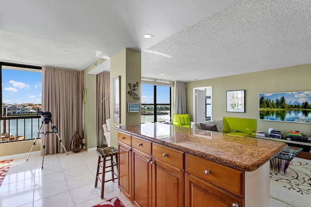 kitchen with light stone countertops, a center island, a textured ceiling, a kitchen bar, and a water view