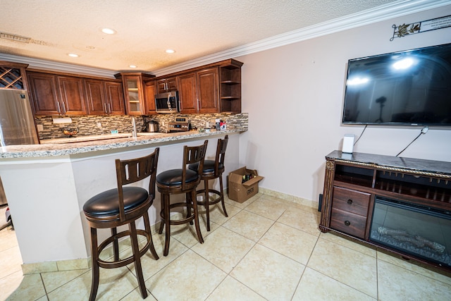 kitchen featuring tasteful backsplash, kitchen peninsula, a textured ceiling, a kitchen bar, and ornamental molding