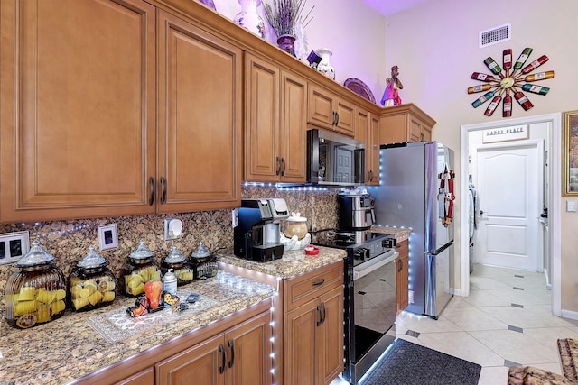 kitchen with appliances with stainless steel finishes, backsplash, light tile patterned floors, and light stone counters