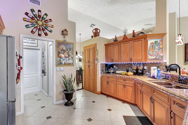 kitchen featuring decorative backsplash, a textured ceiling, sink, stainless steel refrigerator, and hanging light fixtures