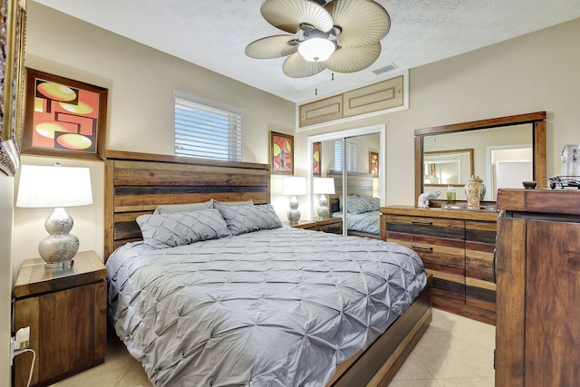 bedroom with a textured ceiling, a closet, ceiling fan, and light tile patterned flooring