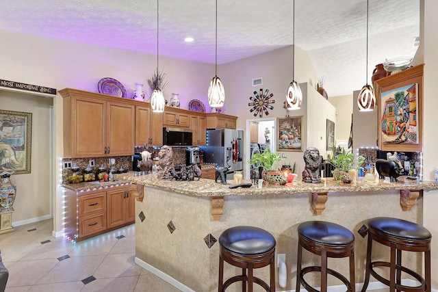 kitchen with hanging light fixtures, light stone counters, a textured ceiling, light tile patterned floors, and appliances with stainless steel finishes