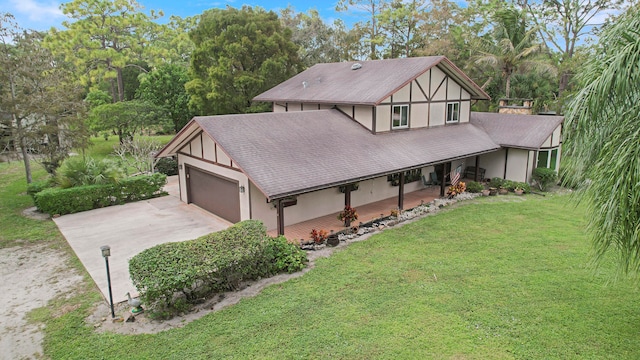 tudor home with covered porch, a front yard, and a garage